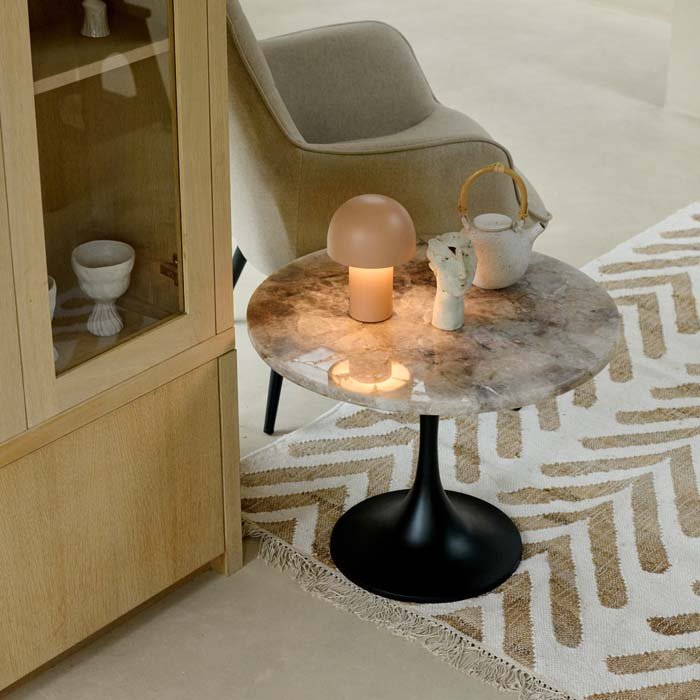 The Stamford Side Table, a simple modern table with a round monochrome marble top, with a warmly lit lamp and accessories.