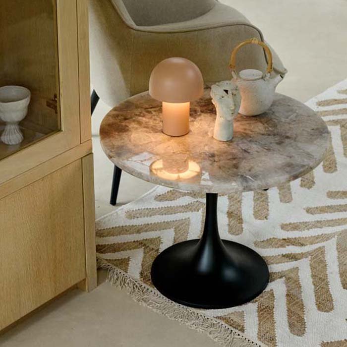 A modern table with a round monochrome marble top, with a warmly lit lamp and accessories.