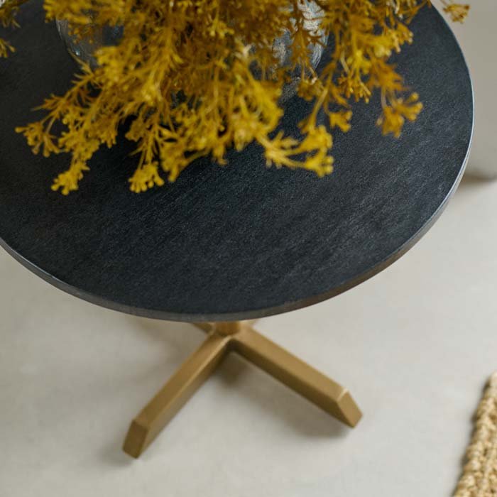 The Varana Round Side Table, with a dark organic shaped stone vase holding some vibrant mustard coloured faux floral stems.