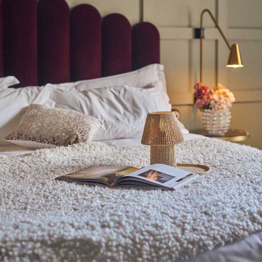 Malone Portable Table Lamp, styled on a bed with a cosy throw.