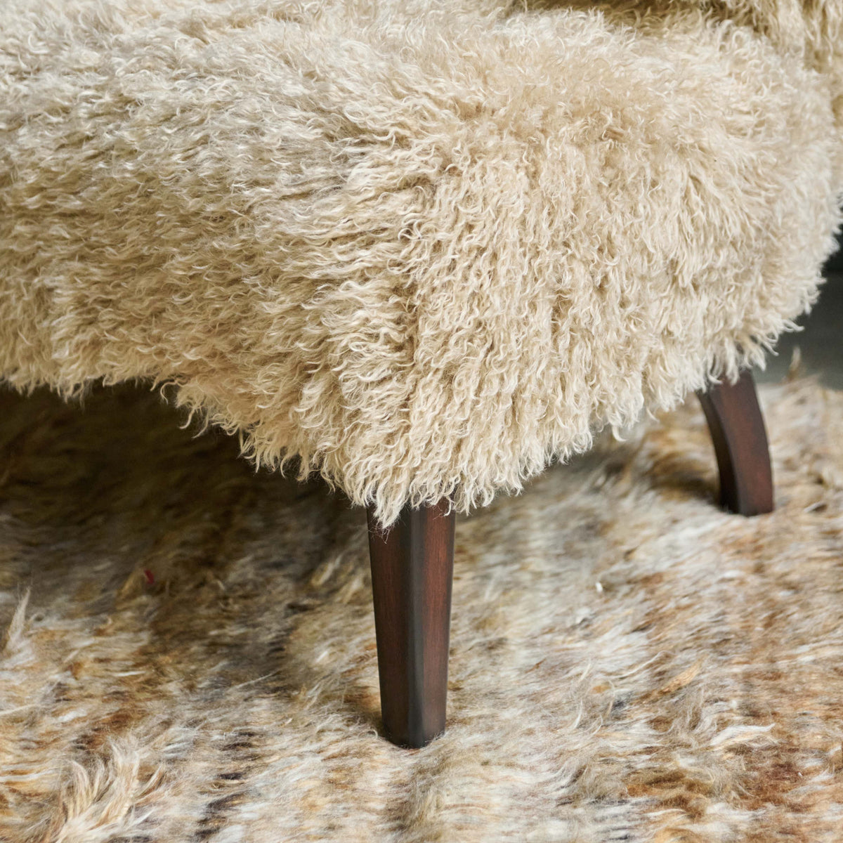 Close up of the wooden legs on a Beige faux fur armchair with a soft textured finish, deep cushioned seat and timeless curved silhouette. Chalford Faux Fur Armchair by Abigail Ahern, designed for ultimate comfort and relaxed lounging while adding warmth and texture to modern interiors. A luxury accent chair perfect for living rooms, bedrooms, reading corners and cosy spaces, creating an inviting statement piece for contemporary home decor.