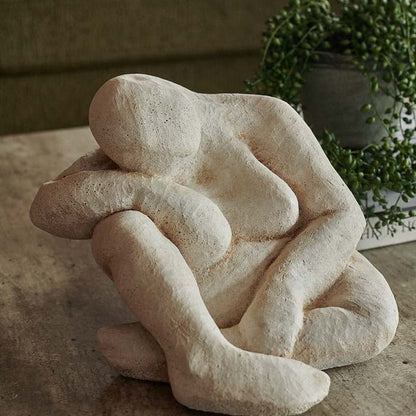 Sitting figurine, with head leaning on right arm and knee, crafted from cement. This figurine is great for home sculpture decor.