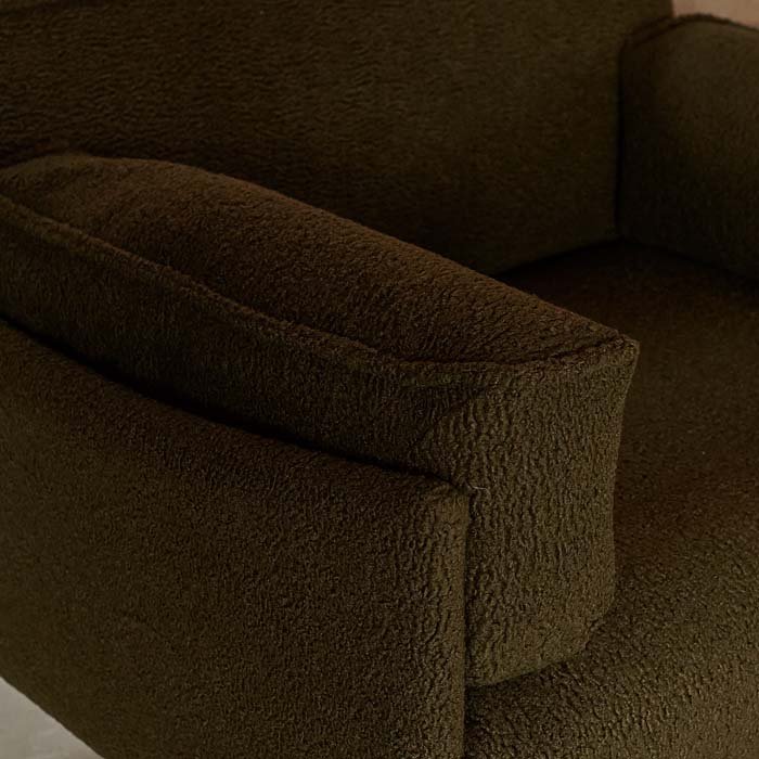 A closeup of the mossy green boucle upholstery on the Eartha Boucle Armchair. Olive green upholstery with a soft textured finish, generous proportions and sleek black iron legs. Eartha Green Boucle Armchair by Abigail Ahern, designed as a contemporary accent chair with a comfortable deep seat and stylish understated silhouette. A luxury statement armchair perfect for living rooms, reading corners and modern interiors, adding rich colour, texture and effortless elegance to your home decor.
