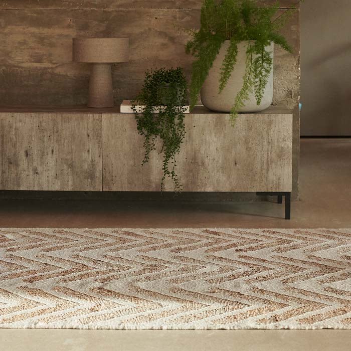 A cream and brown woven rug with geometric arrow design, in front of concrete-look console.
