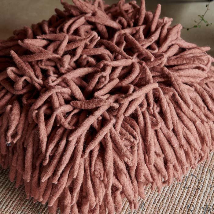 Pinky-red rolled wool tendrils covering a floor cushion.
