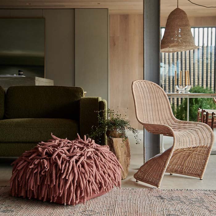 Rust coloured wool floor pouffe next to sculptural rattan chair.