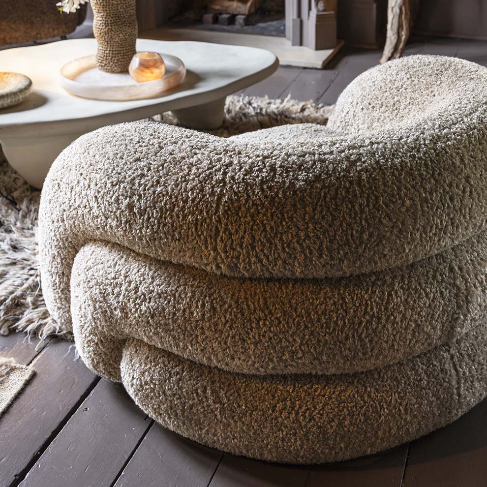 Neutral curved armchair with a plush upholstered finish, rounded silhouette and deep comfortable cushioning. Almar Curved Armchair by Abigail Ahern, designed with a warm earthy tone and contemporary shape to create a stylish statement seating piece. A luxury accent chair perfect for living rooms, bedrooms and cosy reading spaces, adding texture, comfort and timeless elegance to modern home interiors.