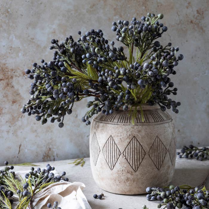 A arrangement of several faux foliage stems with dark blue berries in a patterned ceramic vase.