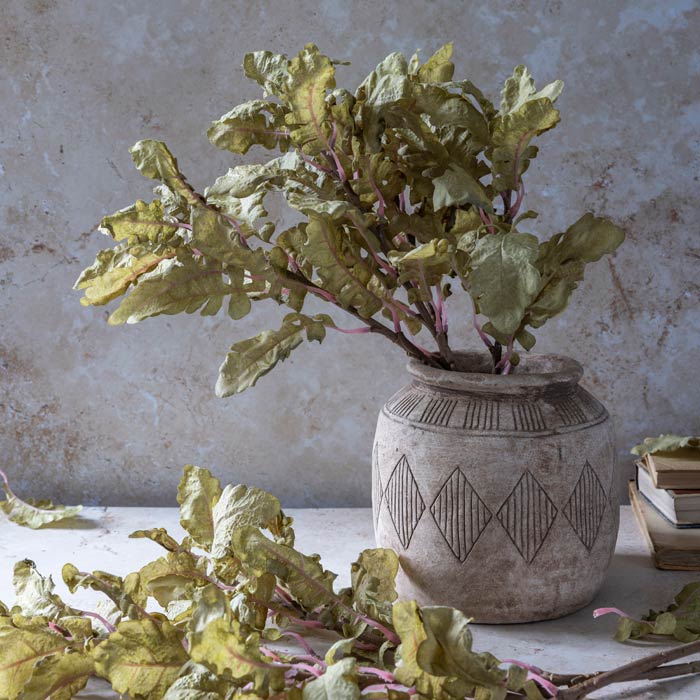 An arrangement of leafy faux foliage arranged in a patterned ceramic vase.