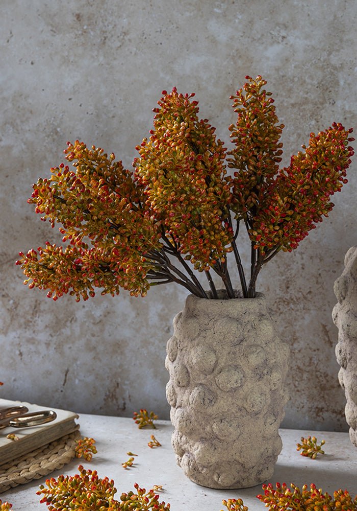 A faux flower bouquet of vibrant artificial orange flower buds arranged in a bobble textured vase.