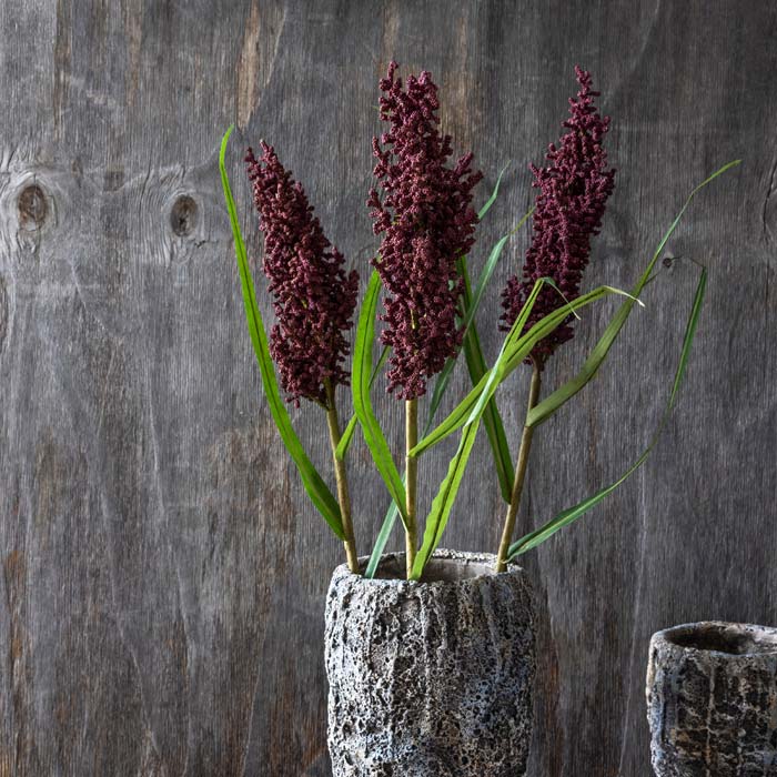A few stems of faux purple flowers arranged in a textural grey vase.