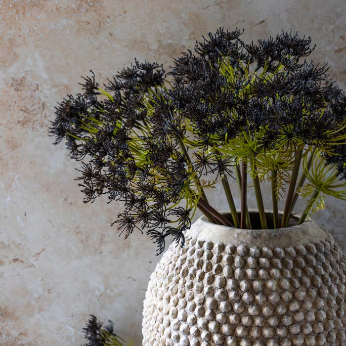 A bouquet of dark blue artificial winter lovage in a bobble textured round vase.