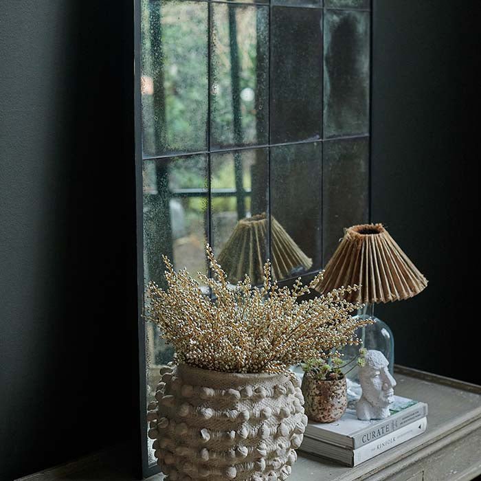 Tall mirror with a thin black frame sat behind a cream vase and table lamp