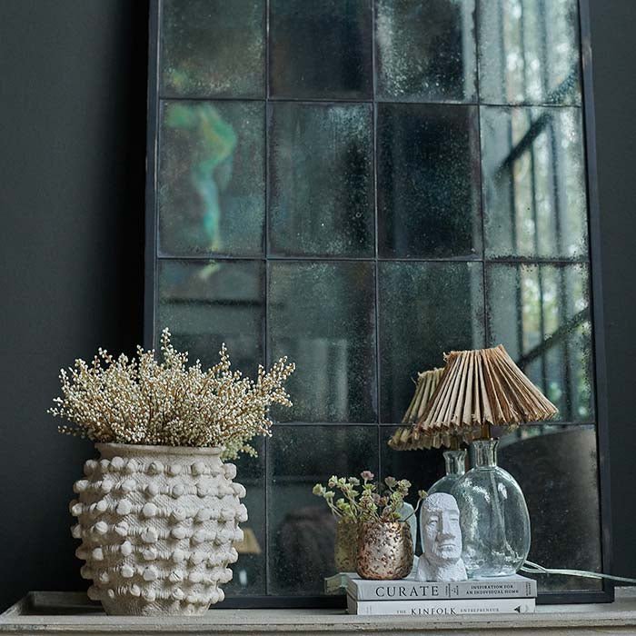 The Aslan Mirror, a tall window pane effect mirror with antique looking glass and a thin black frame, leaning against a wall.