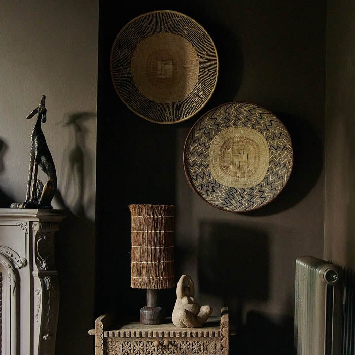 Two round patterned baskets hung on a wall above a table lamp and female sculpture