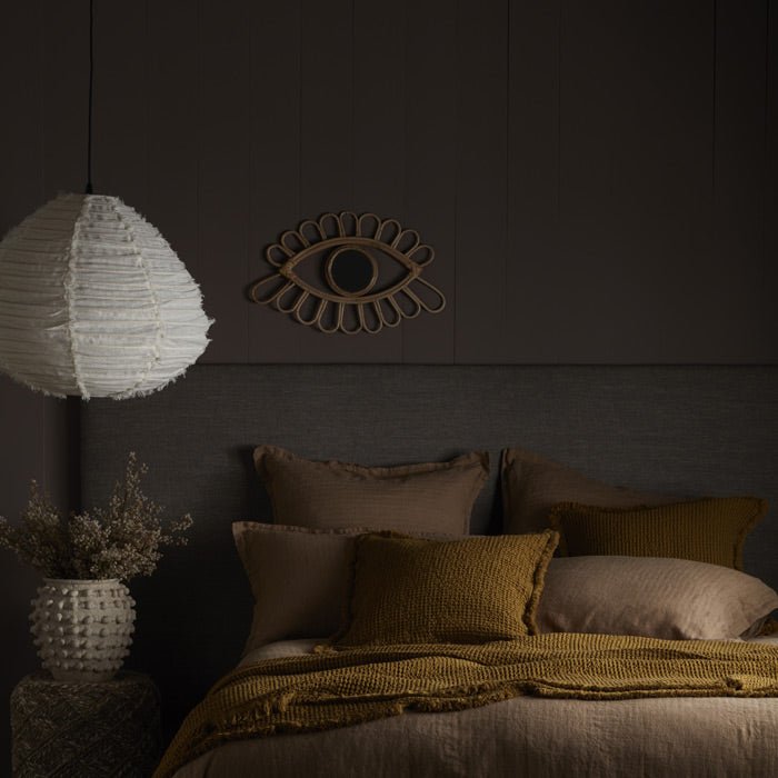 A grey headboard and cream light pendant on a warm brown backdrop