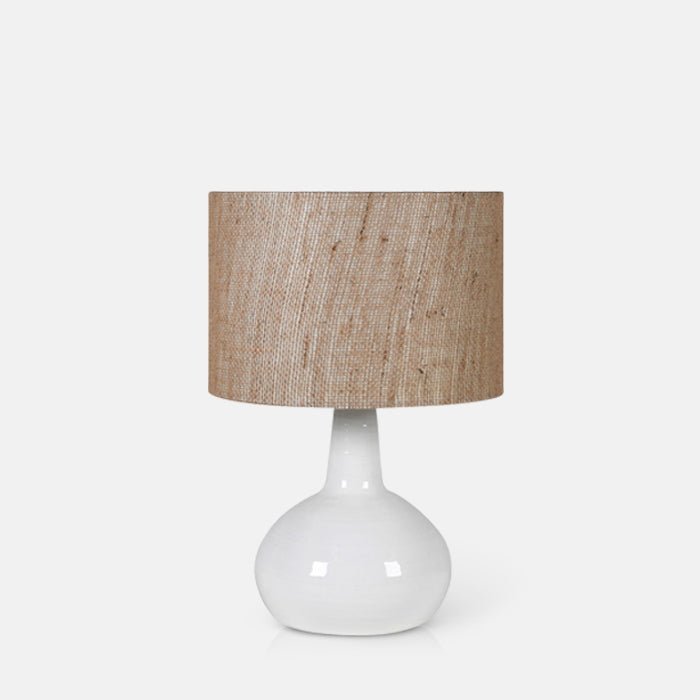 A cutout of the Belvedere Table Lamp, with a white ceramic bulbous shaped base and a woven linen shade.