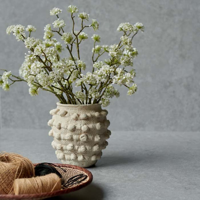 A faux bouquet of artificial stems with small cream flower buds in a bobble textured vase