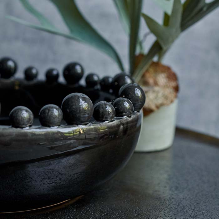The Bourton Bowl - Black, a large round bowl with a glossy glazed finish and textural bubble top, next to a potted fern.