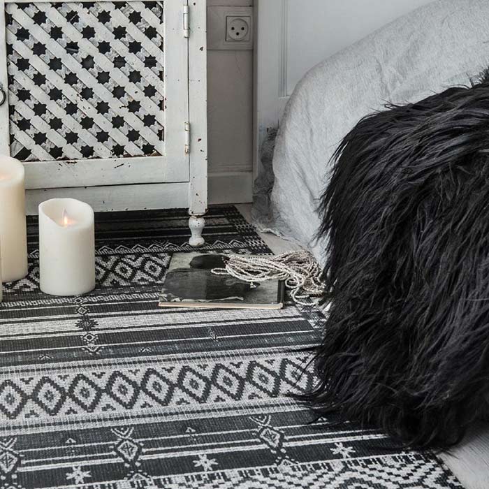 Patterned vinyl rug in a black and white print, sitting next to a bed. Shop premium homeware from Abigail Ahern.