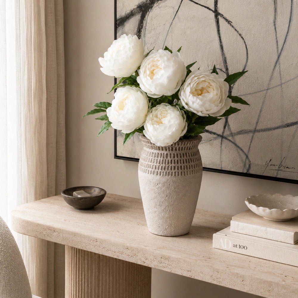 Calstone Cement Vase shown from the front on a styled console, with decorative objects surrounding its sculptural form in a warm neutral interior.
