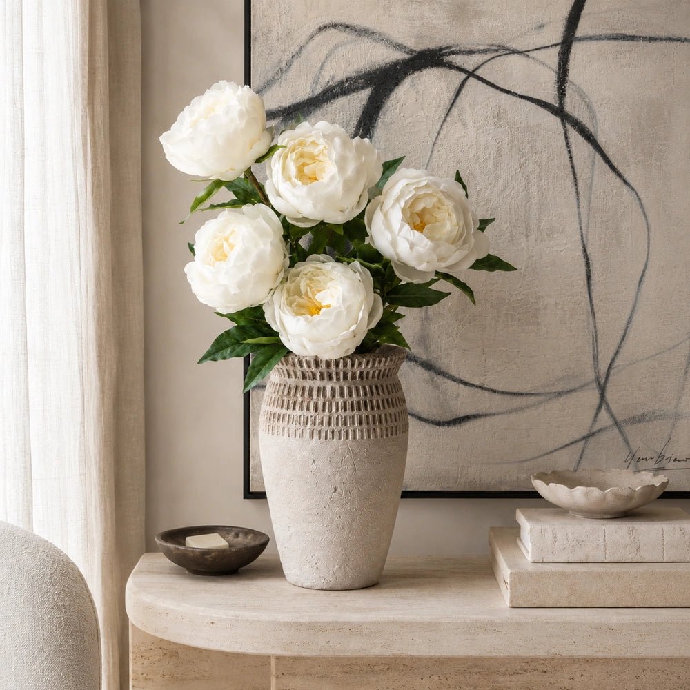 Calstone Cement Vase displayed on a styled console with decorative objects, showing its sculptural rounded form within a warm, softly layered interior setting.