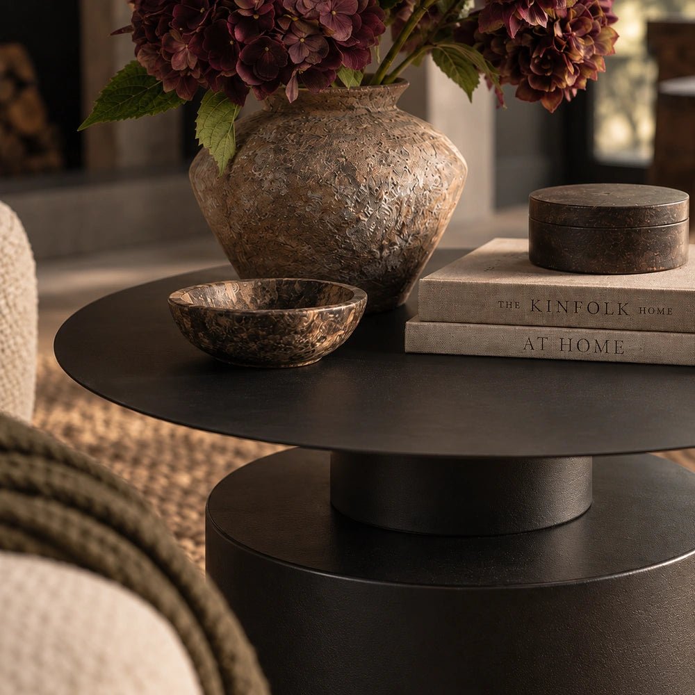 Denholm Metal Coffee Table in a warm living room vignette, styled with a textured vase, dark bowl and stacked books beside soft neutral seating.