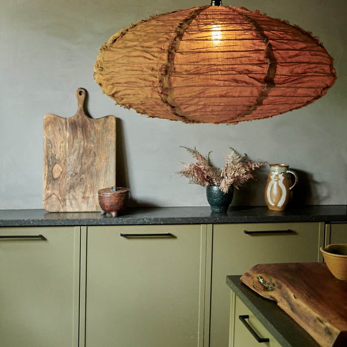 Oval shaped brown fabric pendant shade with a lit bulb hanging in a green and black kitchen. A large linen fabric lampshade to add a designer style to your home.