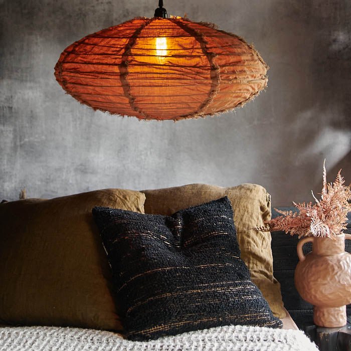 Oval brown fabric pendant light shade switched on above a bed full of cushions