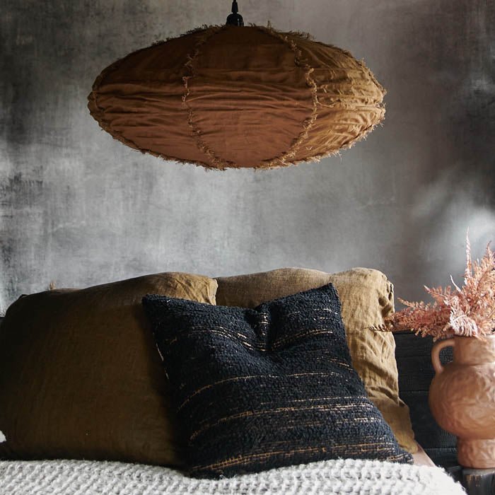 A medium sized linen pendant in a caramel brown colour hung above a bed with lots of cushions. Styling your home for comfort with a touch of chic.