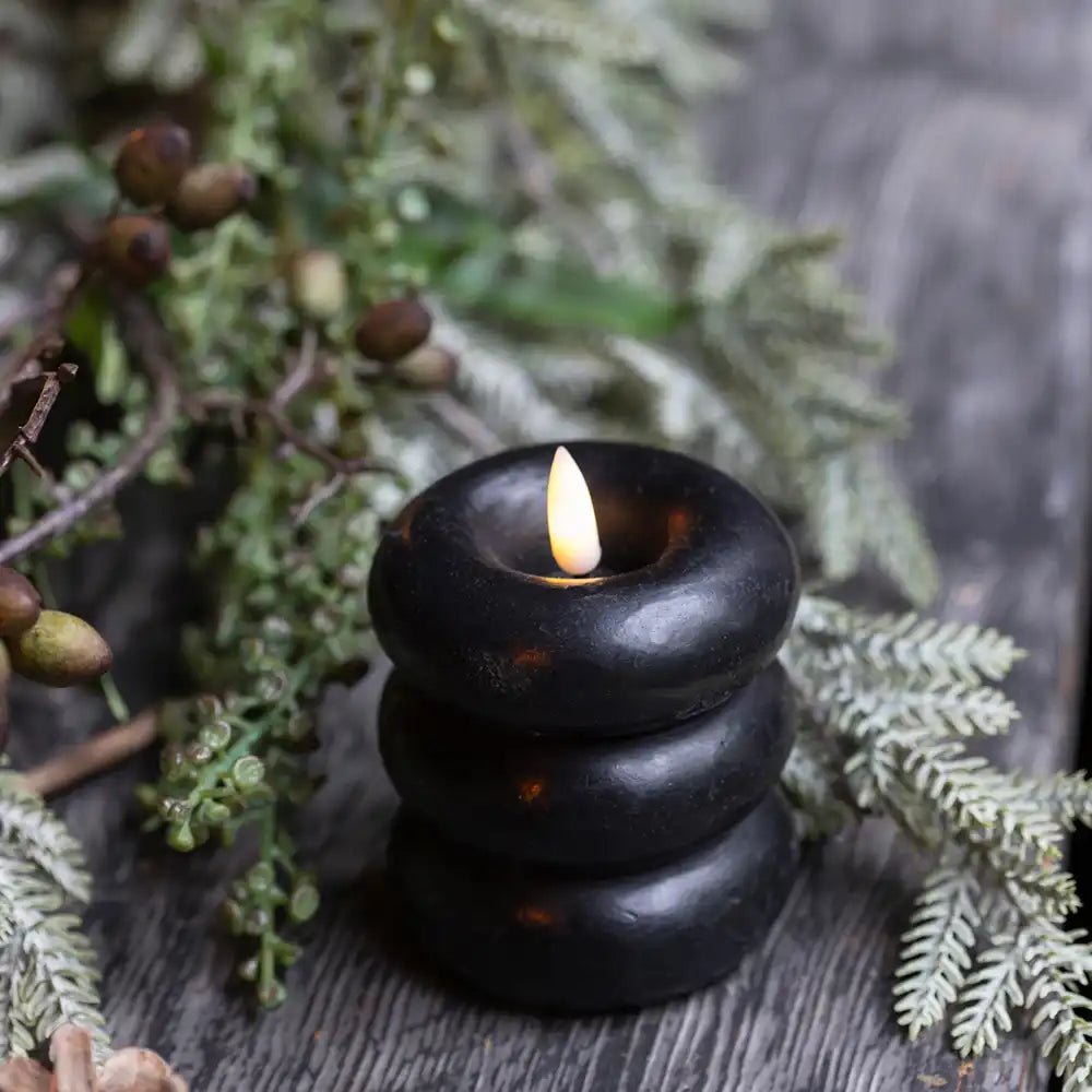 Foley LED Candle - Medium, a black battery candle sitting in some faux plants on a dining table