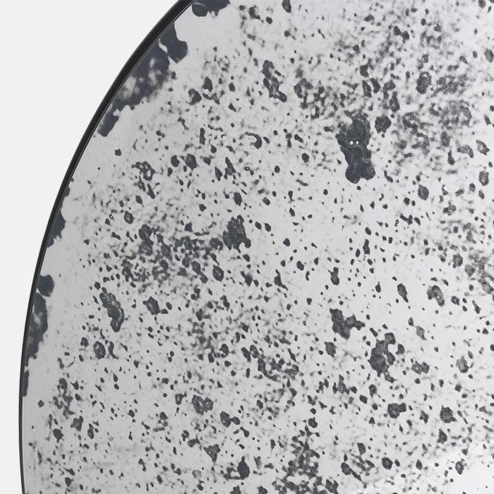 A closeup of the Hyde Antiqued Mirror, a large round mirror with a sleek black frame, featuring antiqued glass.