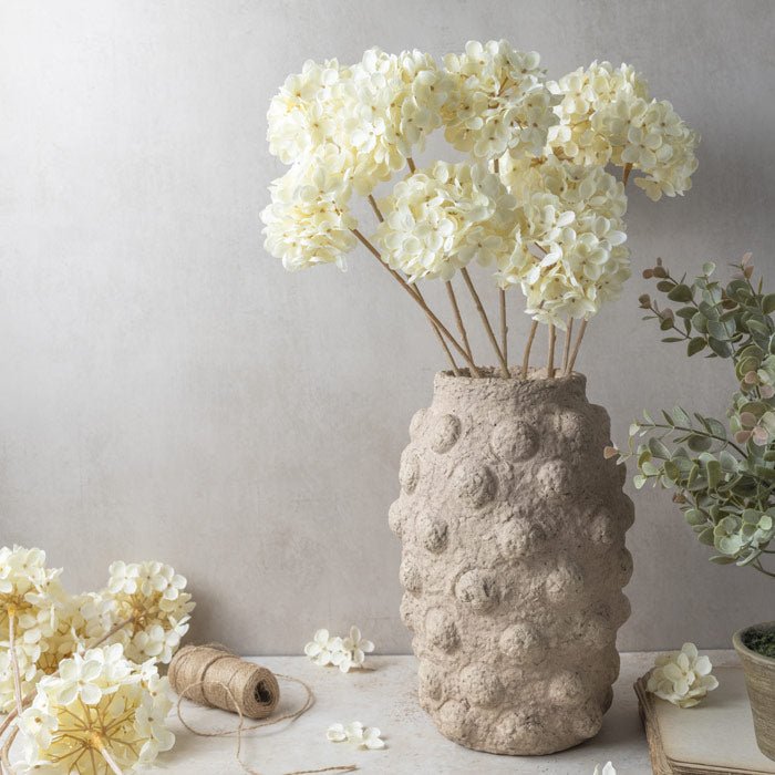 Soft, cream colour faux Hydrangeas styled as a bunch in a rustic ceramic vase. Makes any space feel stylish and thoughtful.