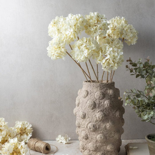 Image of a faux flower bouquet of hydrangeas in a soft cream colour, styled in a textured Abigail Ahern vase.