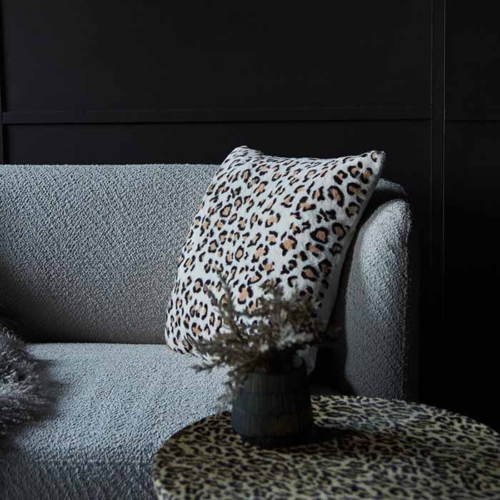 A white square leopard print cushion on a cream boucle sofa.