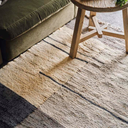 Detail of a cream grey and navy linear block patterned rug with a wooden stool on it