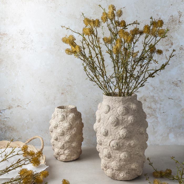 Several stems of artificial meadow pom pom with textural orange flower heads in a bobble textured cement vase.