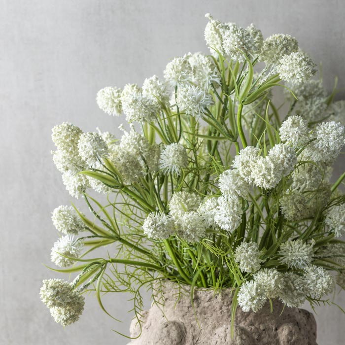A bouquet of faux meadow thistle bush with round white floral heads and green stems in a bobble cement vase.
