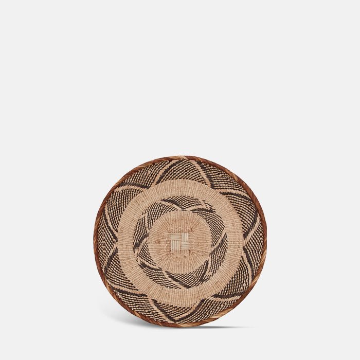 The Melina Basket, a circular shallow woven basket with a geometric tribal pattern.