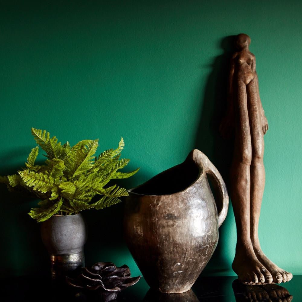 Bold rich green painted wall behind a tall sculpture and artificial green fern