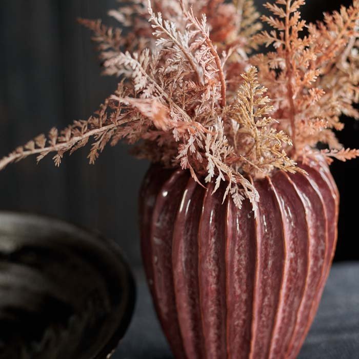 Mollie Ceramic Vase, a rective glazed ceramic vase with a ribbed texture in a dark pink hue styled with some rusty ferns.
