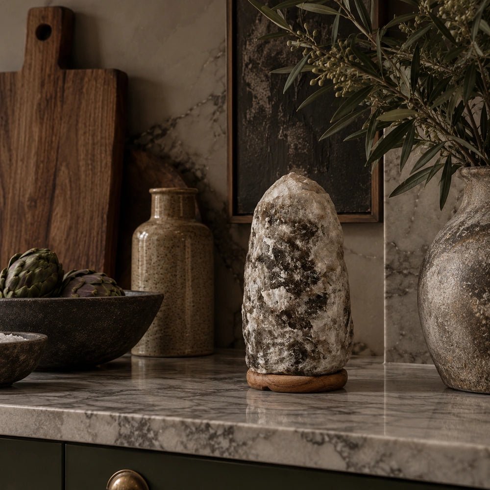 Nepal Natural Salt Lamp in smoky grey crystal, styled unlit on a kitchen counter beside ceramic bowls, wooden boards, foliage and neutral textured accessories.
