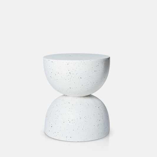 Cutout image on a white background of a speckled white side table. This modern side table has a curved, hourglass shaped and works both inside and outside.