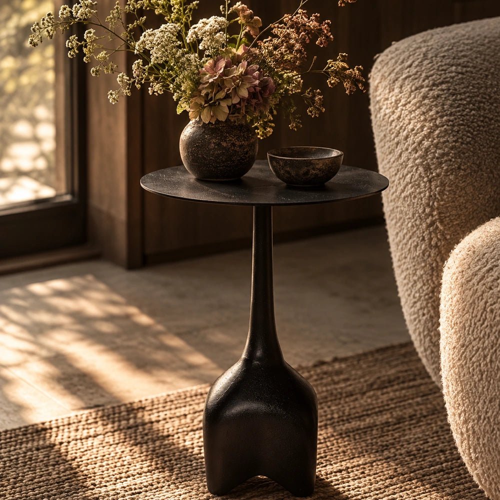 Oren Side Table in black with a sculptural rounded metal silhouette, styled beside a neutral sofa with decorative objects in a warm contemporary living room.