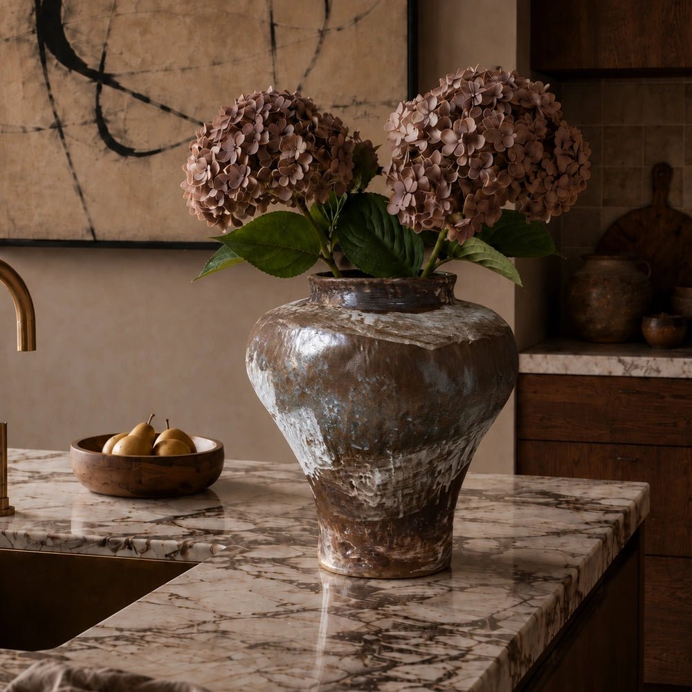 Pedro Ceramic Vase styled with deep burgundy foliage on a wooden surface, highlighting its warm earthy glaze, rounded body and tactile sculptural texture.