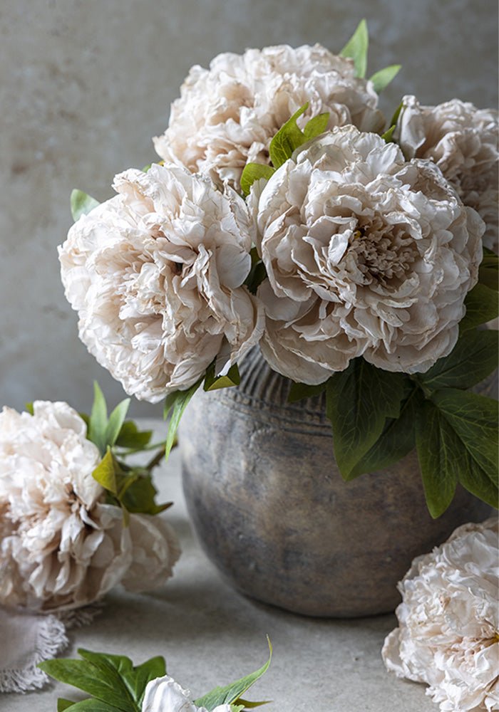 A bouquet of pale pink faux peonies in a round grey vase.
