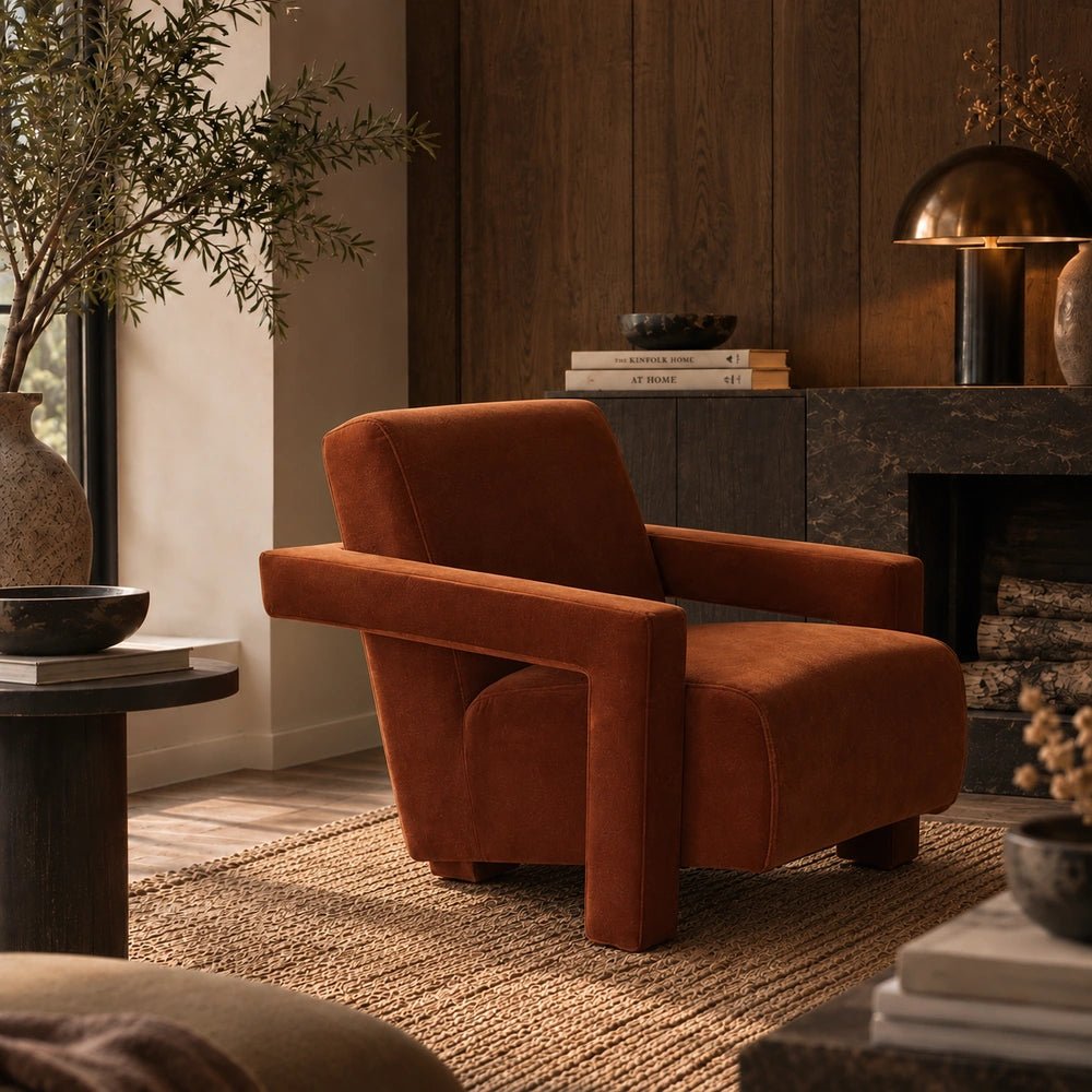 Phoenix Velvet Armchair in burnt orange velvet, styled beside a round side table with decorative objects, patterned rug and warm contemporary living room furnishings.
