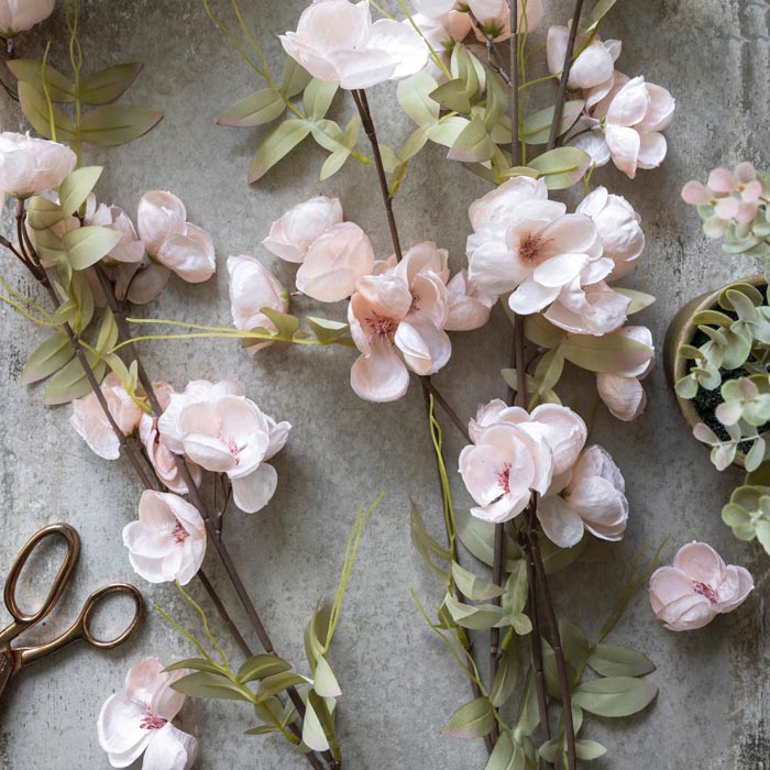 Pale pink floral stems with pale green leaves lying on a table.