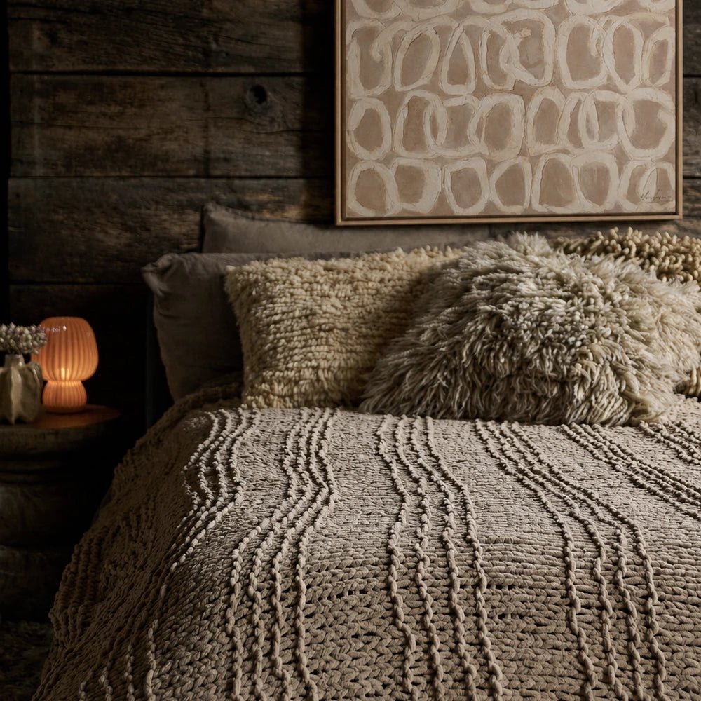 Ripple Canvas Art with soft neutral abstract circular forms in a slim frame, displayed above a layered bed with textured cream cushions and bedding.