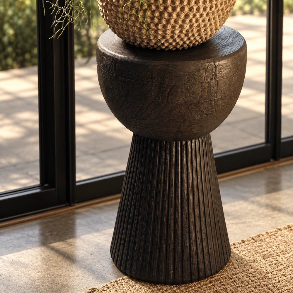Ronan Black Side Table with sculptural rounded top and fluted pedestal base, styled beside a window with a woven vase in a warm neutral interior.